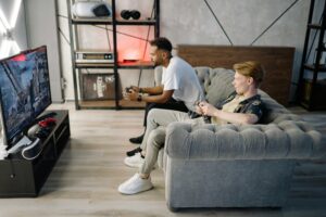 Two adult men playing video games on a couch, enjoying leisure time indoors.